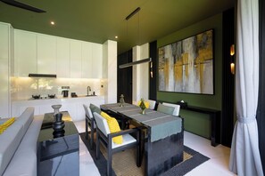 A modern kitchen with white cabinets, a dining area with a glass table, and a large abstract painting on the wall. - Sunset Lagoon Rice Field Villa  (Ubud)