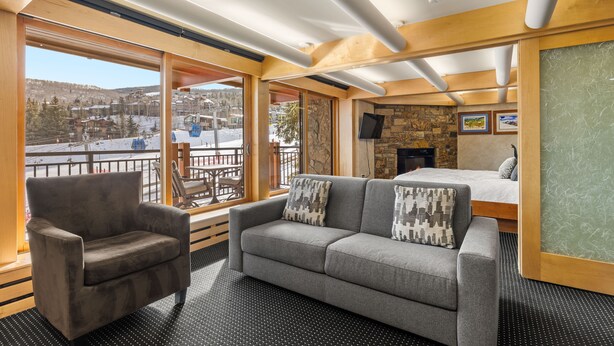 A cozy room with a sofa, armchair, and a bed. Large windows offer a view of a snowy landscape. - Stonebridge Condos 1 Bdrm, Direct ski-in/ski-out (Snowmass Village)