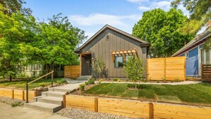 Una casa moderna con techo inclinado, un porche delantero y un pequeño jardín frontal con cerca de madera y algunos árboles.