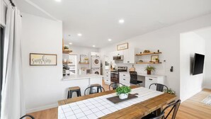 Una cocina moderna con armarios blancos, una mesa de comedor de madera y un televisor instalado en la pared.