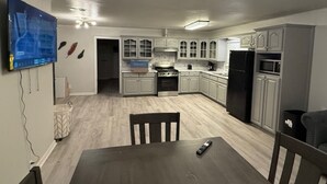 Una cocina moderna con armarios blancos, una mesa de comedor y un televisor montado en la pared.