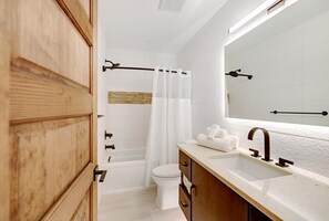 A modern bathroom with a wooden vanity, a large mirror, a bathtub, and a toilet. - Bali Hai Beach Resort (Holmes Beach)
