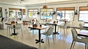 A spacious indoor area with multiple seating arrangements, including tables and chairs, and large windows providing views of the outdoors. - Bali Hai Beach Resort (Holmes Beach)