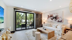 Un salon moderne doté d’une grande porte-fenêtre coulissante donnant sur un balcon, d’un canapé blanc, d’une table basse et d’un tableau accroché au mur.