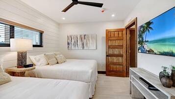 Habitación de hotel con dos camas, un ventilador de techo, un televisor de pared que muestra una escena de playa y una puerta de madera.
