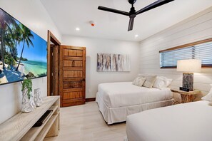 A bedroom with two beds, a ceiling fan, a beach view through a door, and a painting on the wall. - Bali Hai Beach Resort (Holmes Beach)