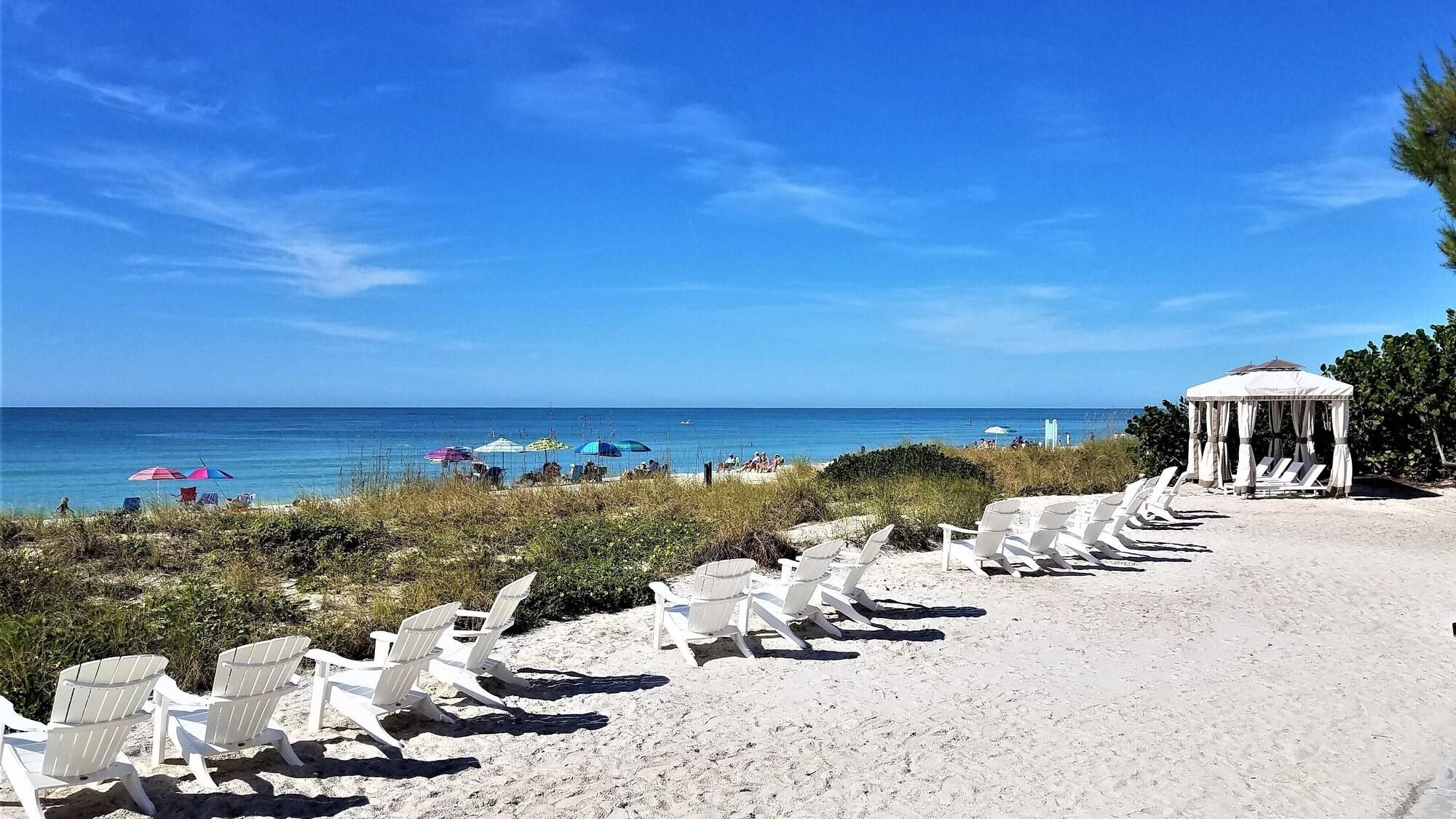 Uma praia com cadeiras de praia brancas e um gazebo.