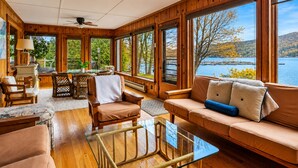 Eine Holzhütte mit großen Fenstern, einem Glastisch und einer Couch mit Kissen.