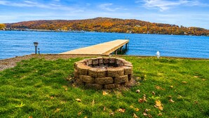 Blick auf einen See mit einer Holzsteg, einer Feuerstelle aus Stein und einer Rasenfläche.