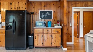 A kitchen with wooden cabinetry, a black refrigerator, a microwave, and a chalkboard sign. - 3 Mins to Watkins Glen | Seneca Wine Trail (Watkins Glen)