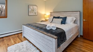 A bedroom with a wooden bed, a white rug, a nightstand with a lamp, and a framed picture on the wall. - 3 Mins to Watkins Glen | Seneca Wine Trail (Watkins Glen)