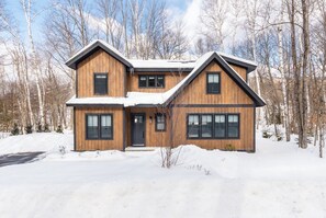 Una casa de madera de dos pisos con un diseño simétrico, ventanas grandes y un techo cubierto de nieve.