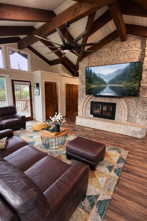 A spacious living room with a stone fireplace, a large flat-screen TV, and a leather couch. - Resort-Style Retreat ~ Pool • Hot Tub • Theater • Game Room • Sauna • Acreage  (Arlington)