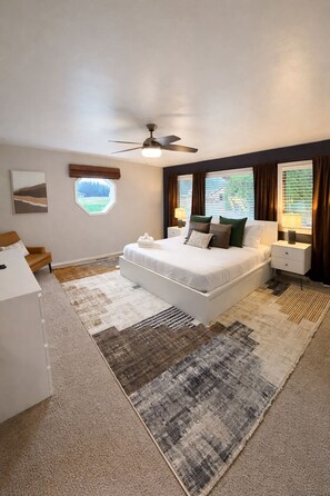 A modern bedroom with a large bed, a desk, and a ceiling fan.