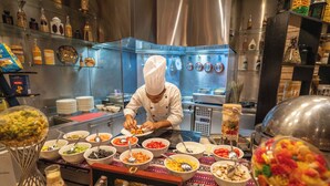 Un chef preparando comida en una cocina moderna con electrodomésticos de acero inoxidable y varios alimentos a la vista.