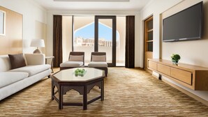 Una habitación de hotel moderna con un ventanal grande, un televisor de pantalla plana, un sofá, dos sillones, una mesa de centro y una consola de madera.