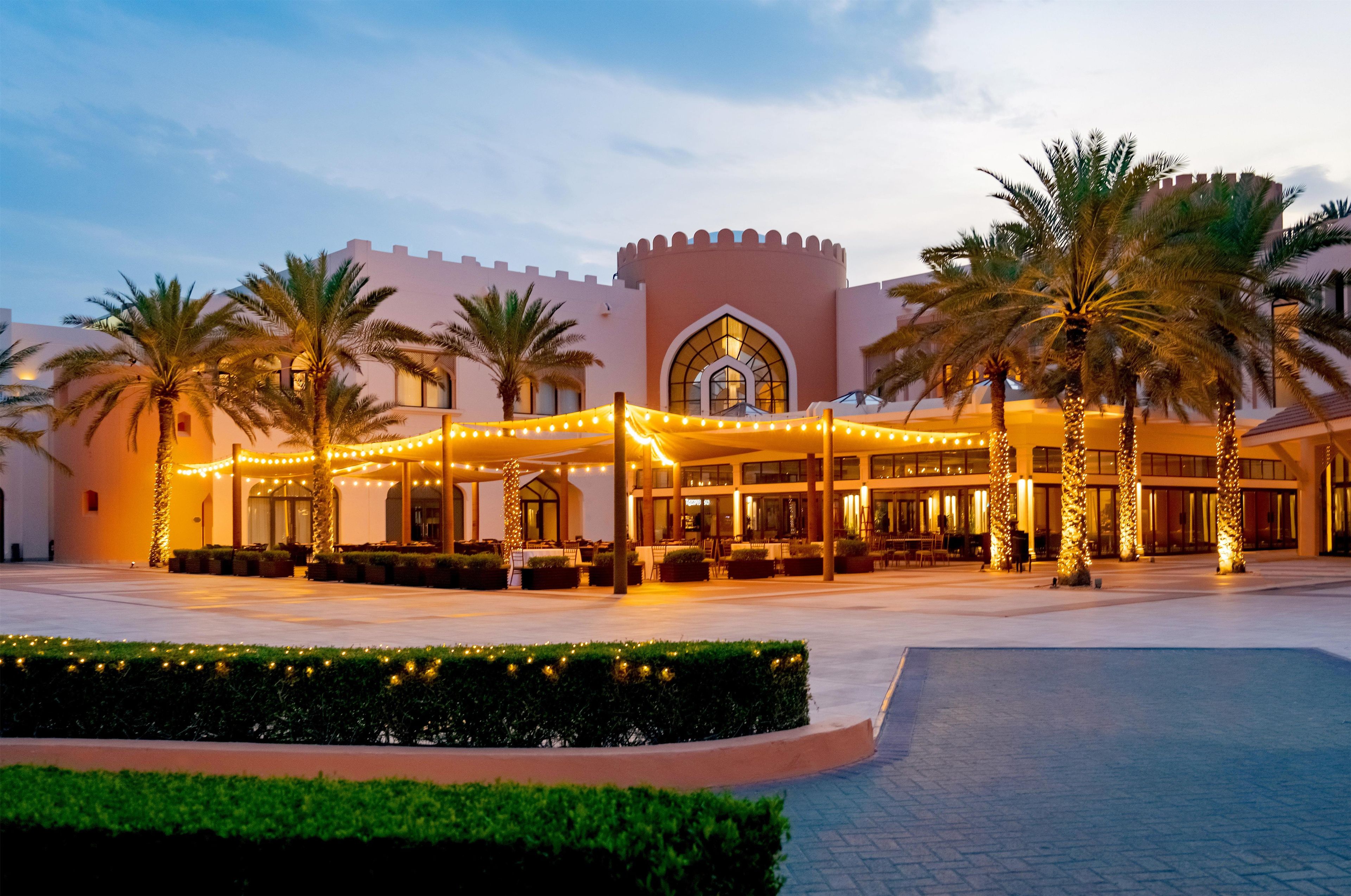 A hotel with a courtyard, palm trees, and string lights.