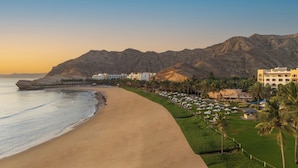 Un resort costero con playa de arena, palmeras y montañas al fondo.