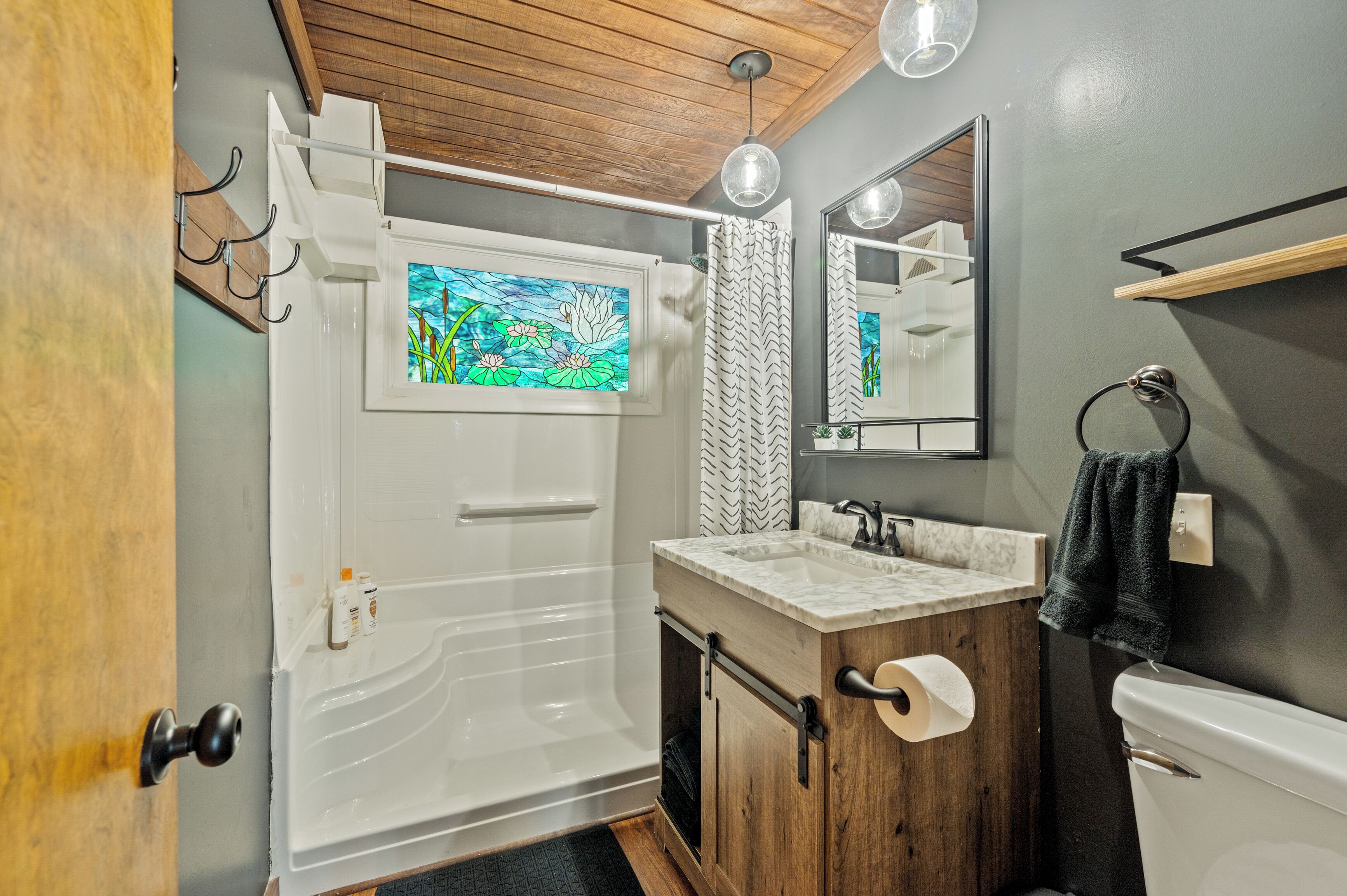 Un bagno con un mobile lavabo in legno, una vasca da bagno bianca, una tenda da doccia, uno specchio e un porta asciugamani.