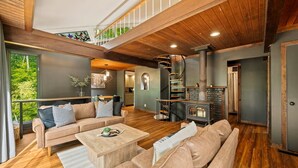Amplia sala de estar con escalera de madera, chimenea y balcón con vistas a zonas verdes.