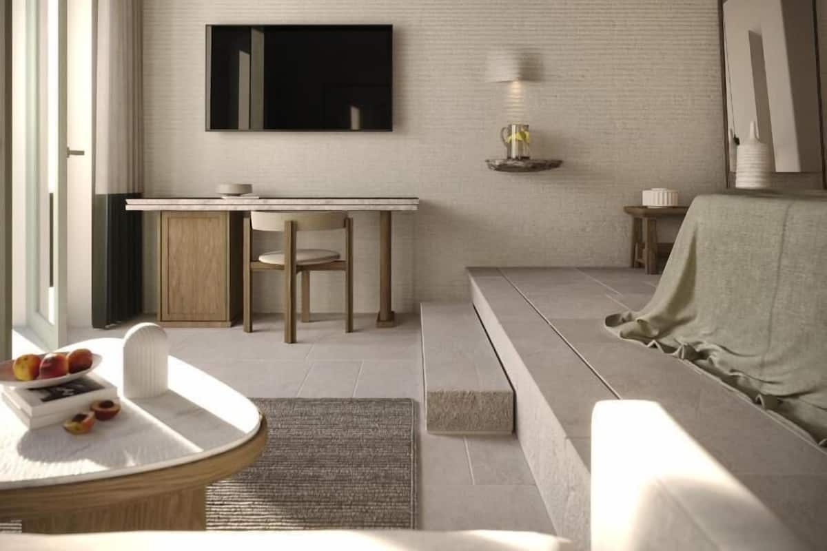 Un salon moderne comprenant un canapé, une table à manger avec des chaises, une table basse avec des fruits, un téléviseur fixé au mur et une lampe sur une table d’appoint.