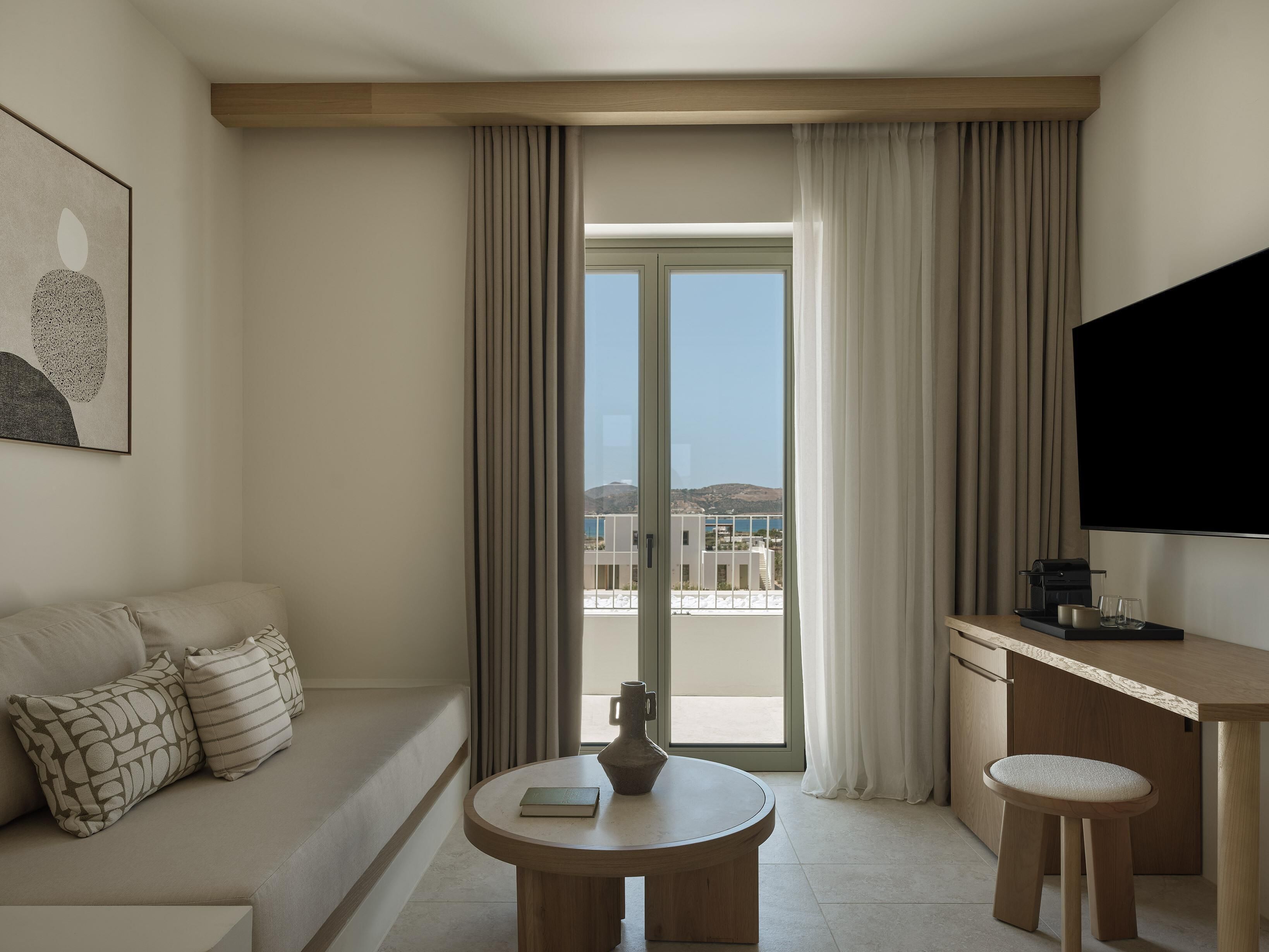 A modern hotel room with a sofa, a small round table, a coffee machine, and a TV.