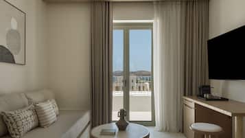 A modern hotel room with a sofa, a small round table, a coffee machine, and a TV.