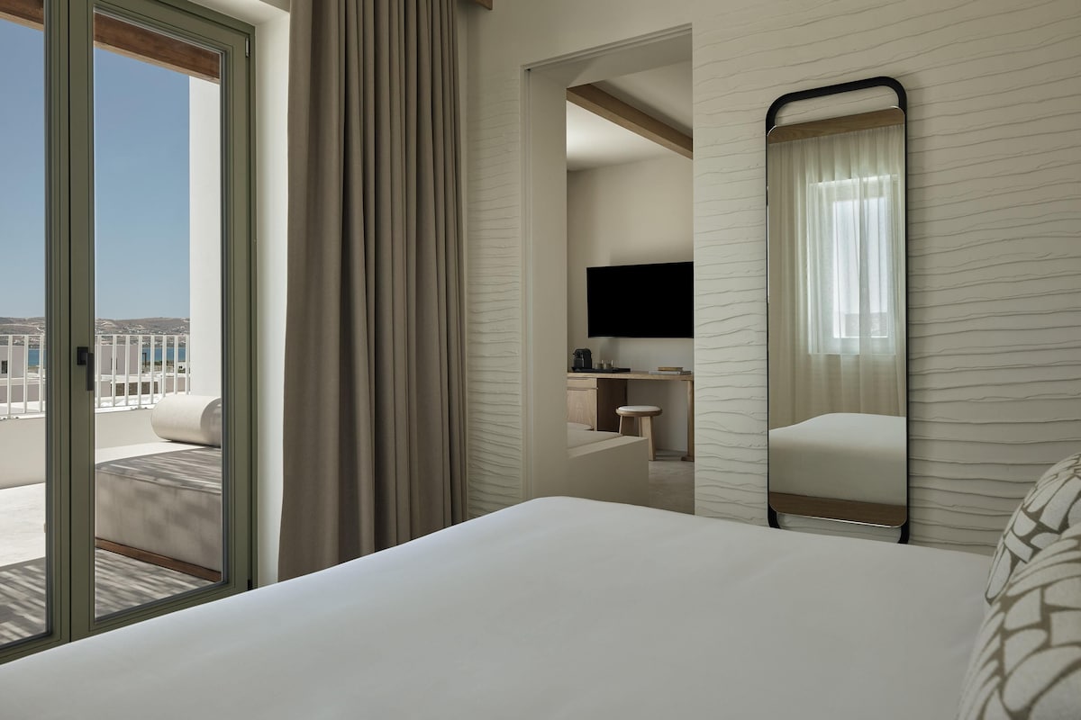 Una habitación de hotel con cama, escritorio con televisor, silla y vistas al exterior.