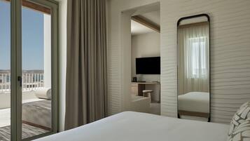 Una habitación de hotel con cama, escritorio con televisor, silla y vistas al exterior.