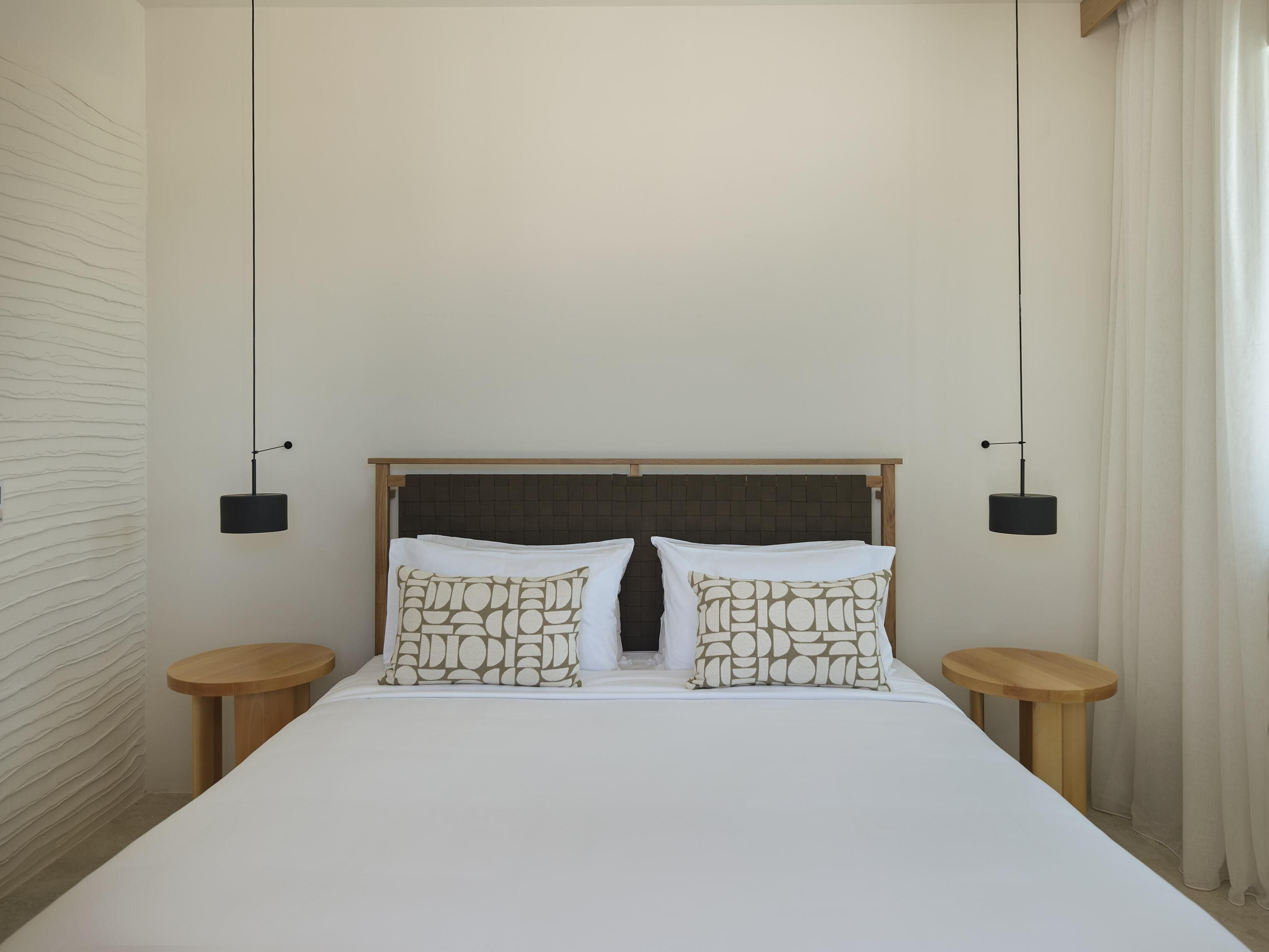 Une chambre d’hôtel avec un grand lit, deux tables de chevet et une tête de lit ornée d’un motif quadrillé.