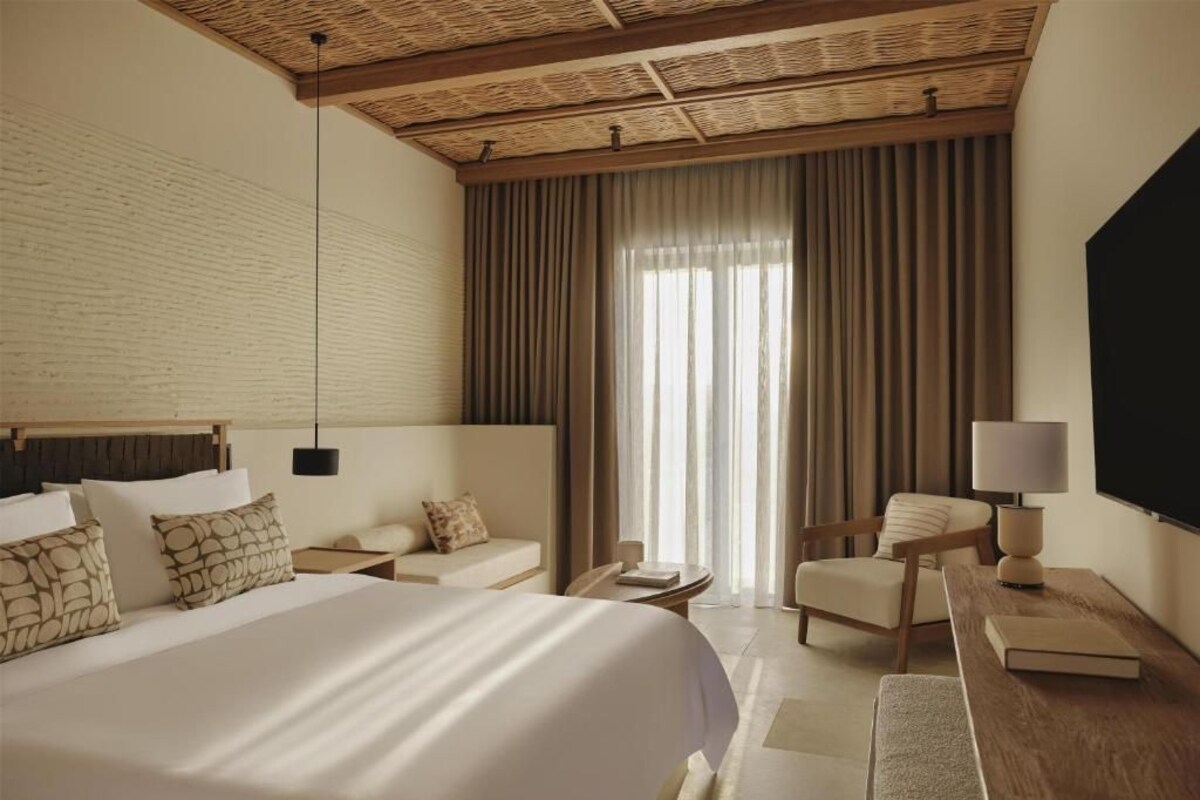 Habitación de hotel con una cama grande, un escritorio, una silla, un televisor y una ventana con cortinas.