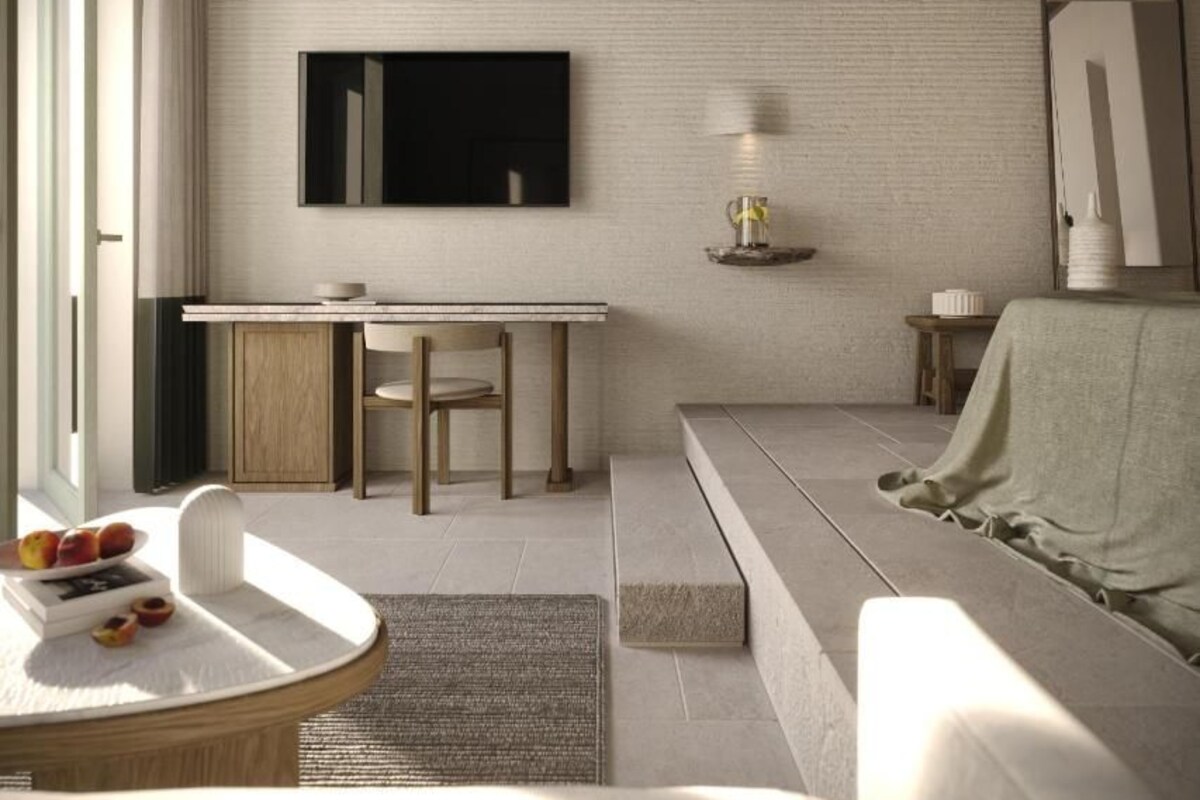 Un salón moderno con un sofá, una mesa de comedor con sillas, una mesa baja con frutas, un televisor montado en la pared y una lámpara sobre una mesita auxiliar.