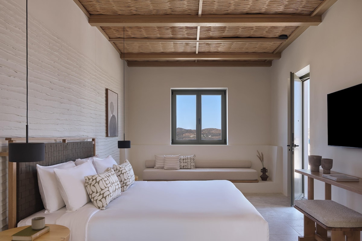 Un dormitorio con una cama grande, una ventana, un televisor de pantalla plana y un banco de madera.