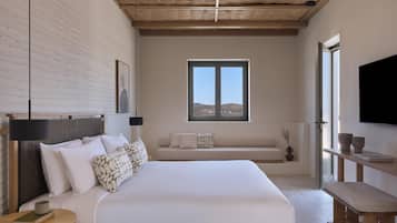 Un dormitorio con una cama grande, una ventana, un televisor de pantalla plana y un banco de madera.