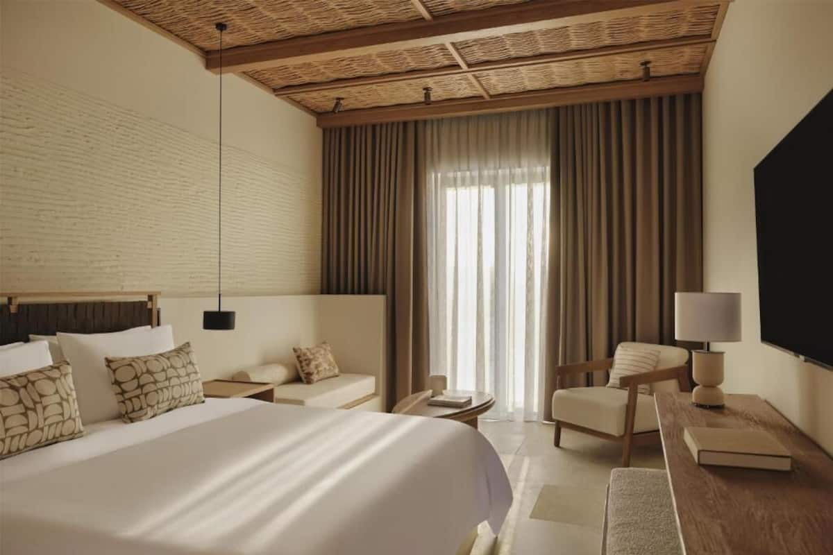 Une chambre d’hôtel avec un grand lit, un bureau, une chaise, une télévision et une fenêtre avec des rideaux.