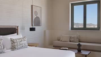 A bedroom with a large bed, a sofa, a small table, and a window with a view of the hills.
