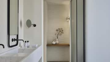 A modern bathroom with a large mirror, marble sink, and a vase with dried flowers on a shelf.