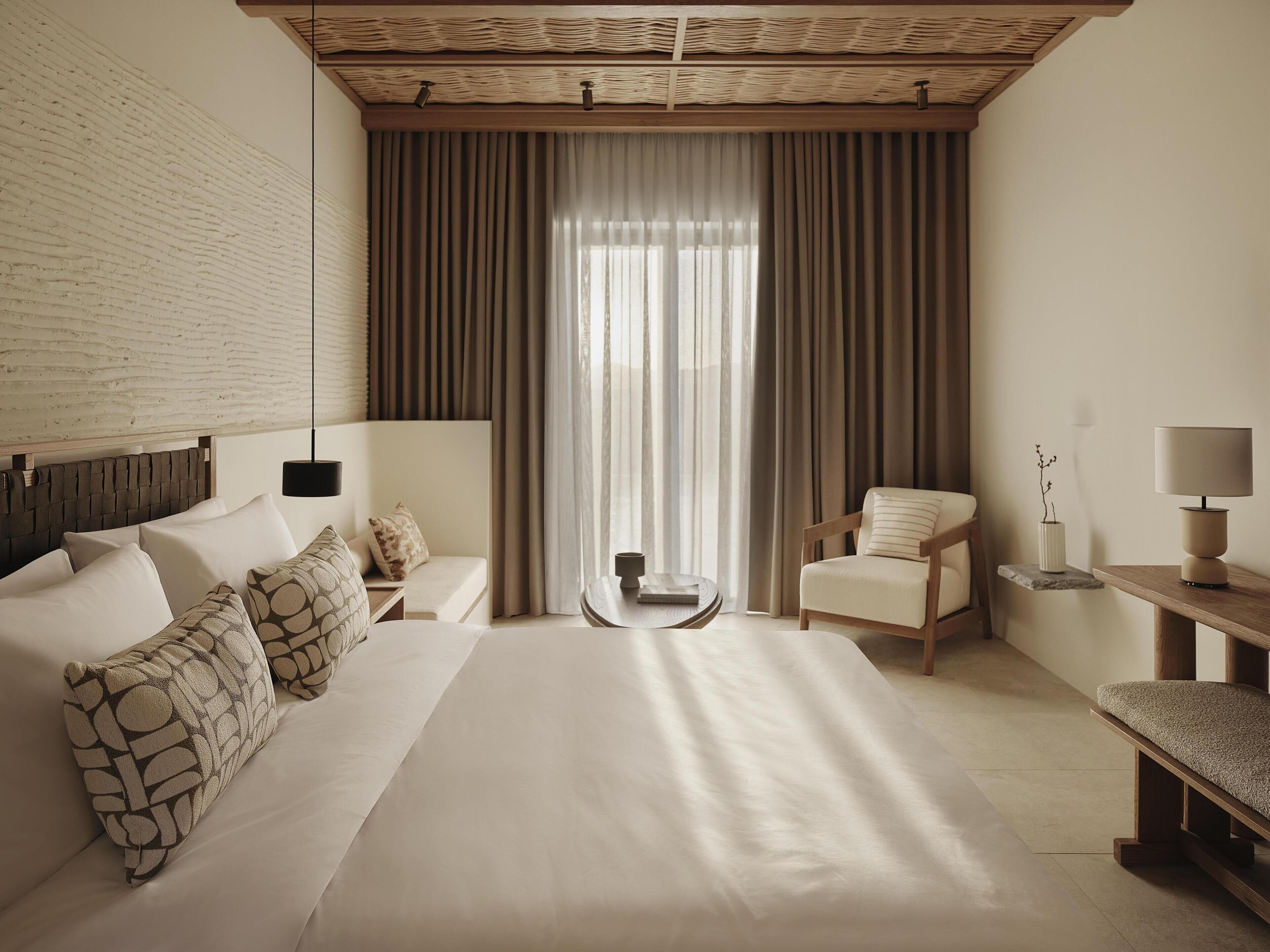 A hotel room with a large bed, a chair, a small table, and a lamp.