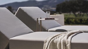 A sun lounger with a glass of water and a book, set against a mountainous backdrop. - Parian Chronicle Hotel Paros, Destination by Hyatt (Paros)