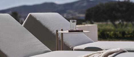 A sun lounger with a glass of water and a book, set against a mountainous backdrop.
