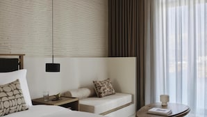 Ein Hotelzimmer mit Bett, Sofa, kleinem Tisch, Nachttisch, Lampe und durchsichtigen Vorhängen.