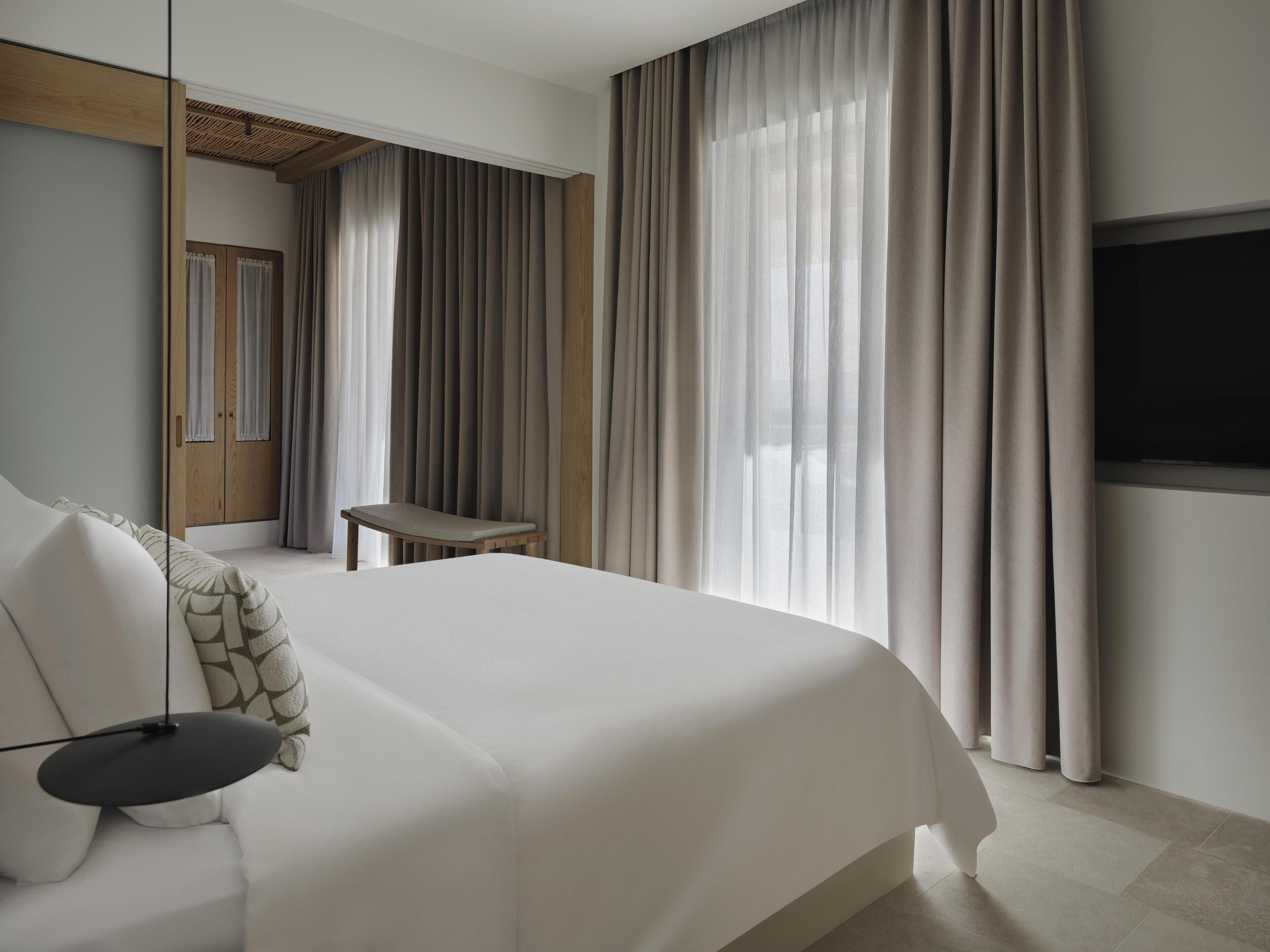Une chambre d’hôtel moderne équipée d’un grand lit, d’un bureau, d’une télévision et d’une armoire.