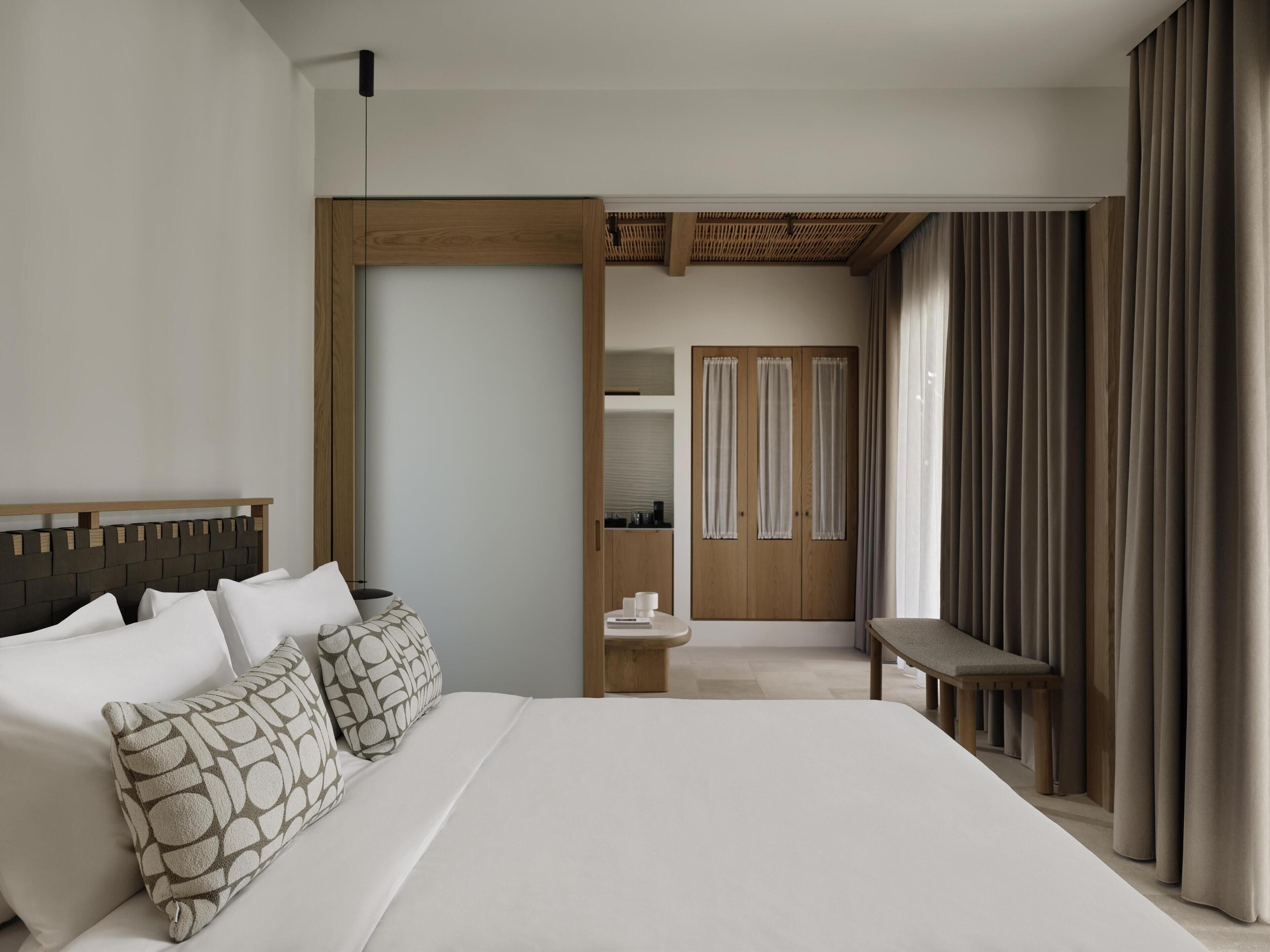 A modern hotel room with a large bed, a wooden headboard, a desk, and a wardrobe.