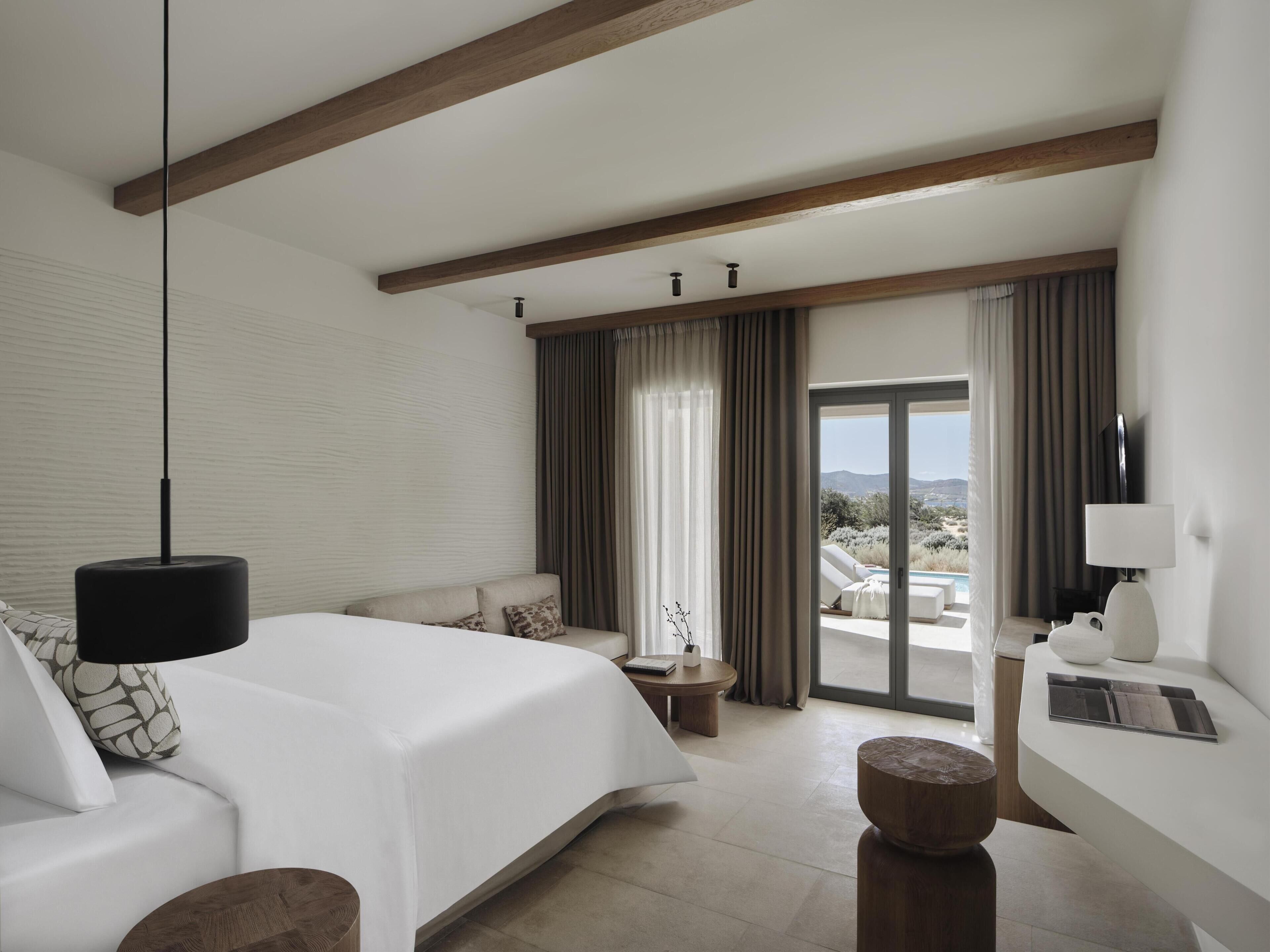 Une chambre d’hôtel avec un lit, un canapé, une petite table, une télévision et une vue sur une piscine et un paysage.