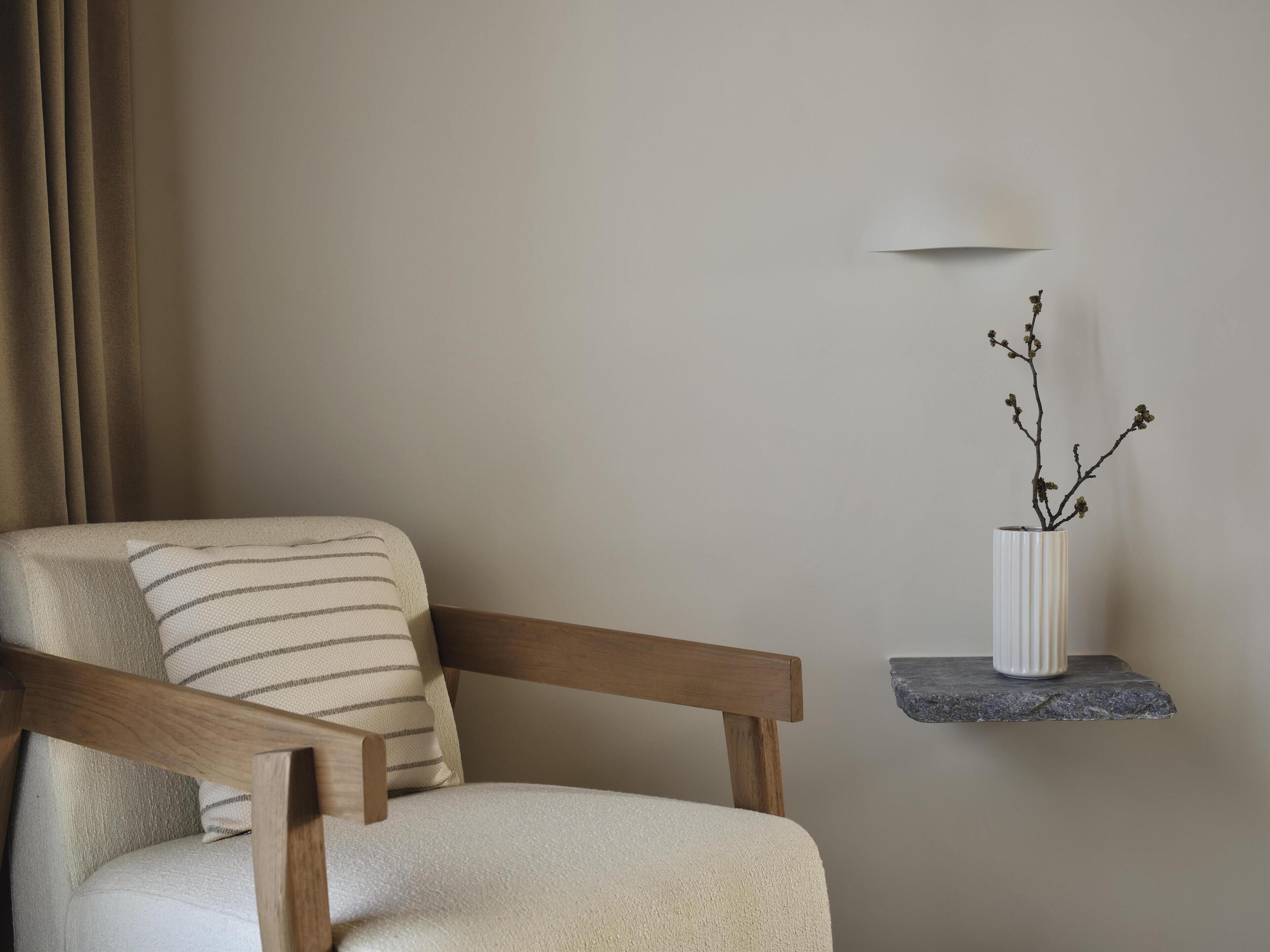 A chair with a striped pillow, a vase with a branch, and a wall-mounted light fixture.