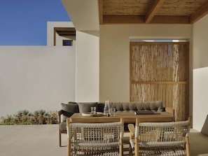 An outdoor patio with a wooden table, wicker chairs, a sofa, and a bamboo screen.