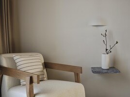 Una silla con un cojín a rayas, un florero con una rama y una lámpara de pared.