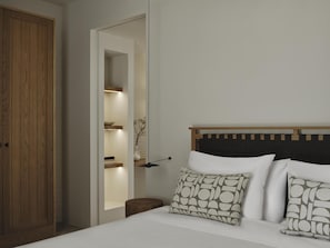 Un dormitorio con un armario de madera, una mesita de noche, una cama con ropa de cama blanca y un cabecero con estampado geométrico.