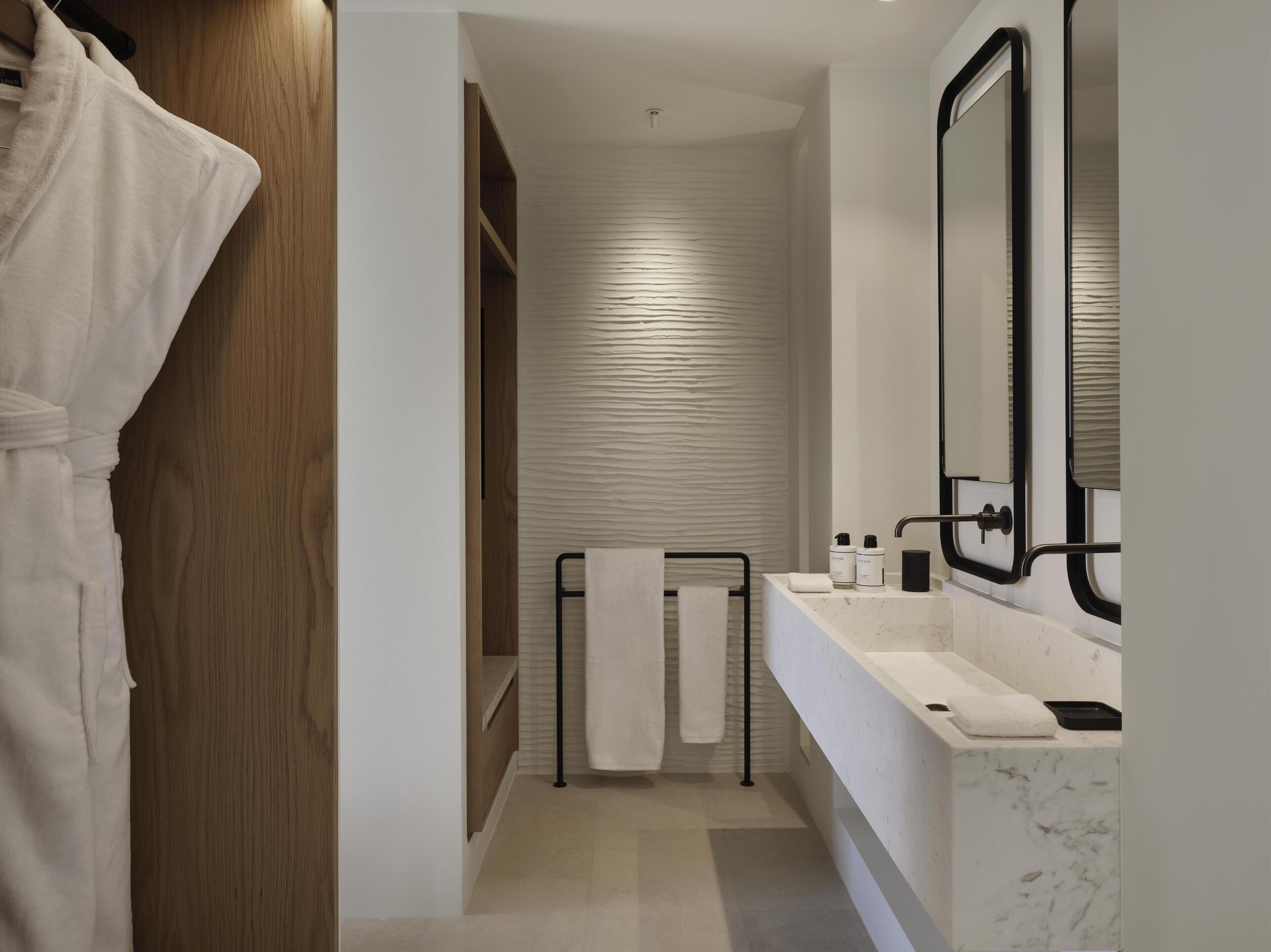 A modern bathroom with a wooden wardrobe, a towel rack, a sink with a mirror, and a shower area.