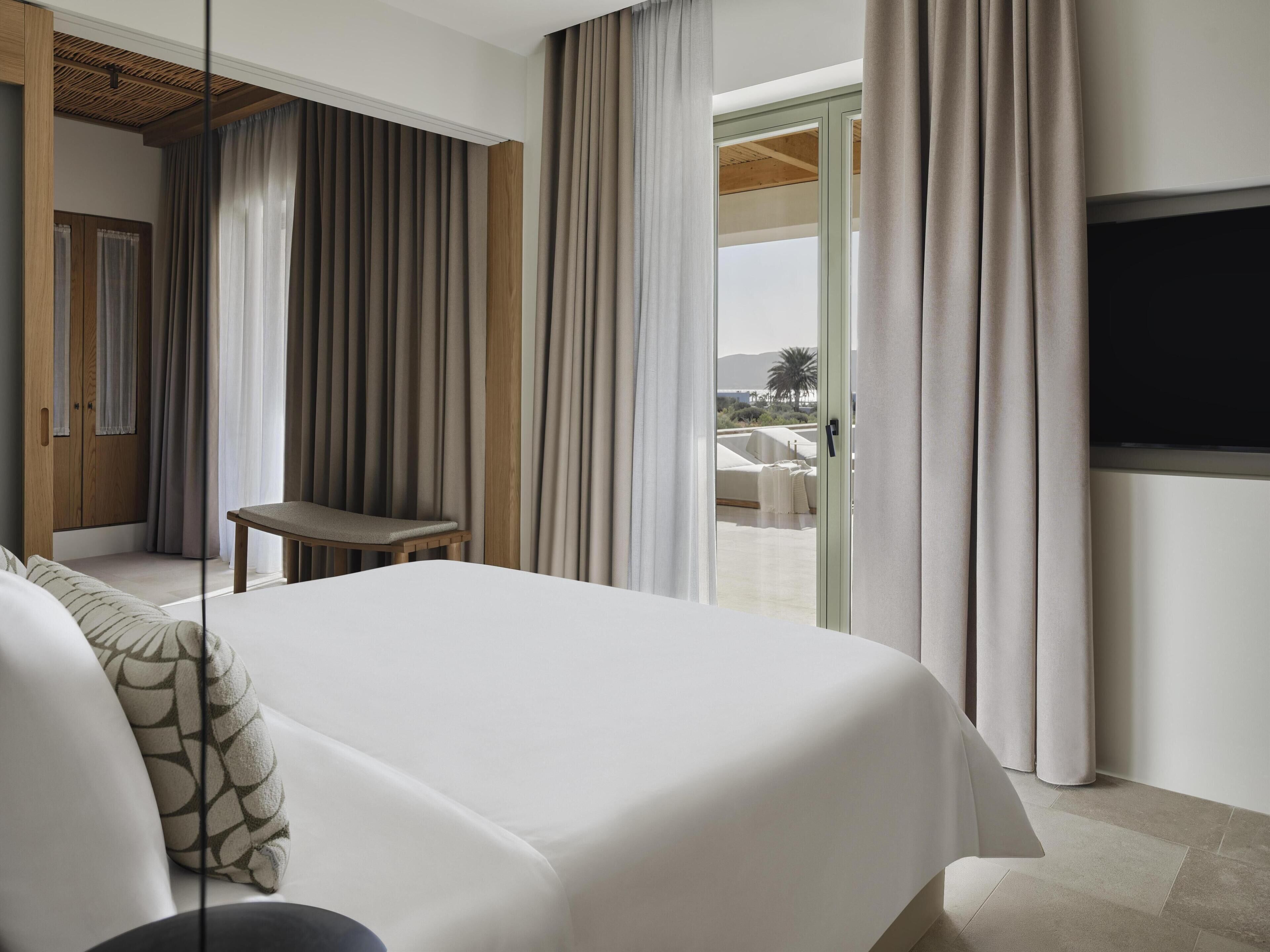 A hotel room with a bed, a seating area, a TV, and a view of the outdoors.